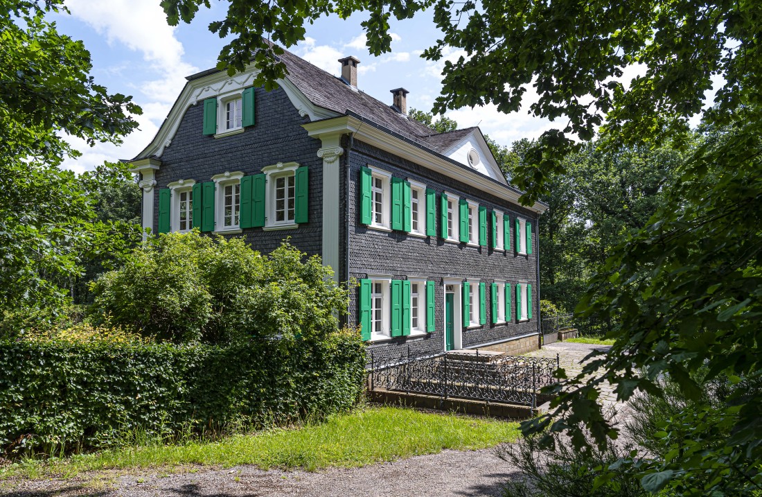 Haus mit grauer Schieferfassade, weißen Fensterrahmen und grünen Fensterläden