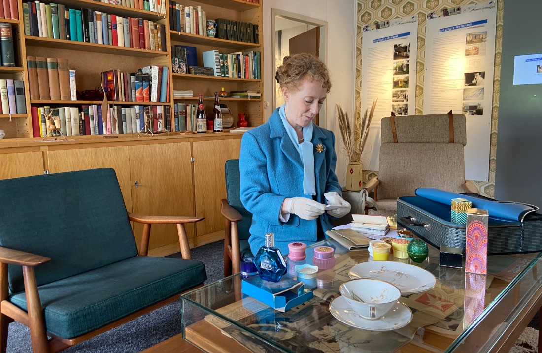 Woman in a blue costume stands in front of a table with cosmetics