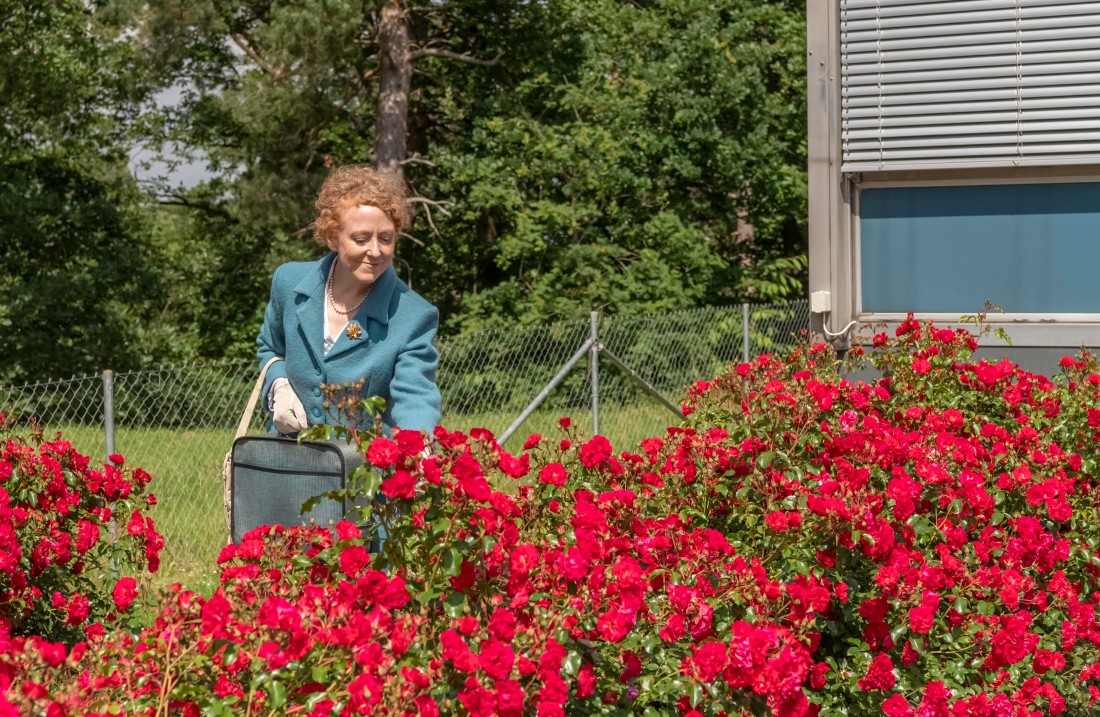 Frau in blauem Kostüm schaut lächelnd auf Rosen