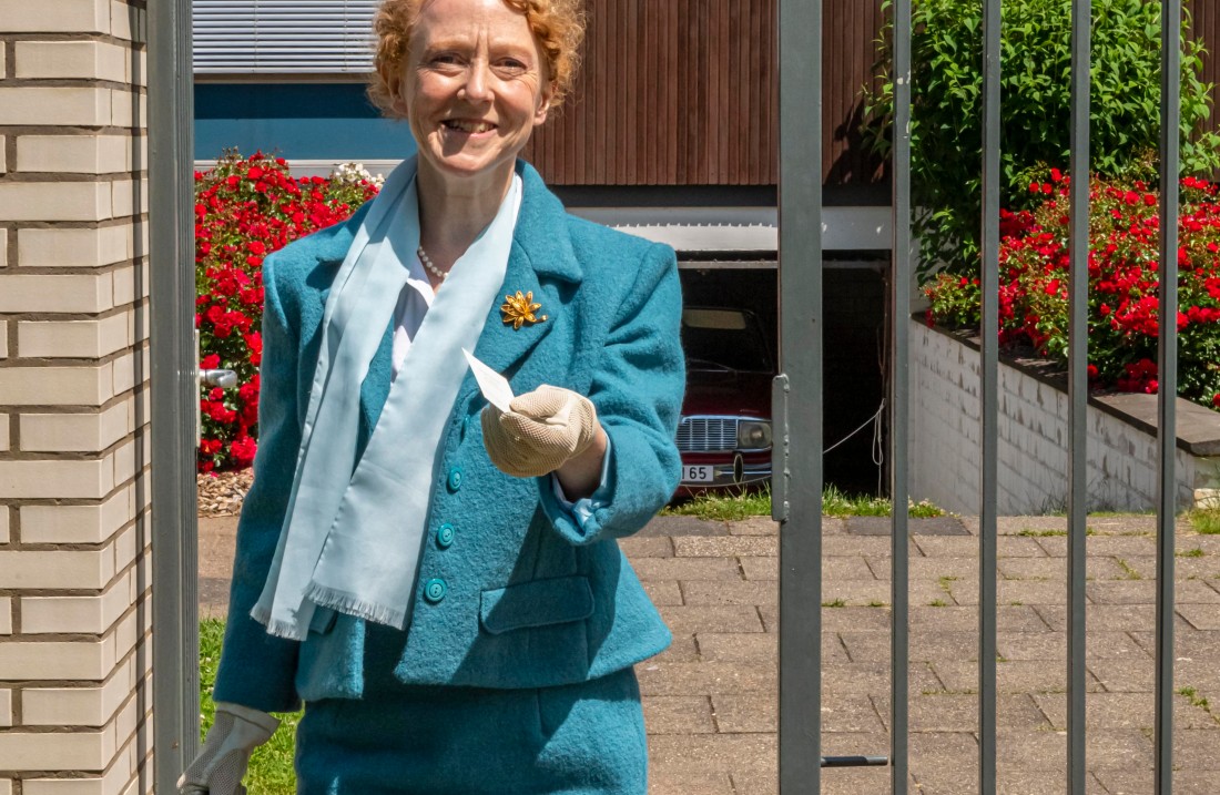 Frau in blauem Kostüm kommt mit einer Visitenkarte auf einen zu.