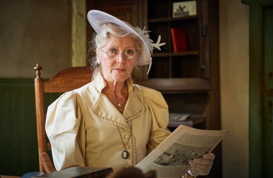 Lady in a chic blouse and hat sits and reads something