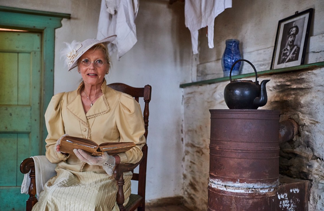 Lady with a hat and a chic blouse with ruffles sits on a chair and reads