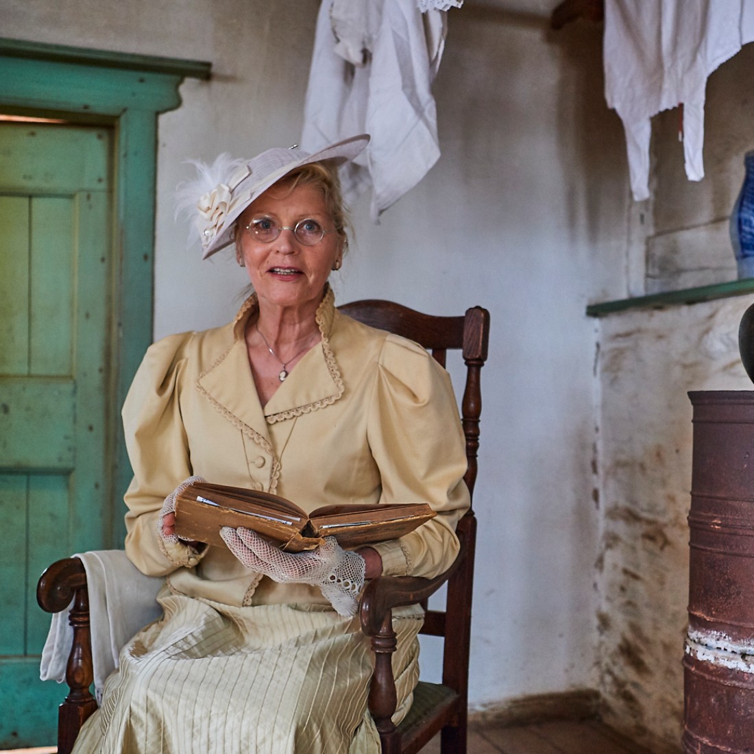 Lady in a hat and chic blouse with frills sits on a chair and reads