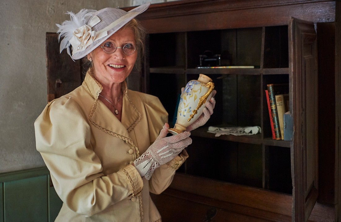 Lady with a blouse and a white hat holds a vase in her hand.