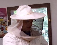 Mann im Imkeranzug steht vor einem Bienenstock