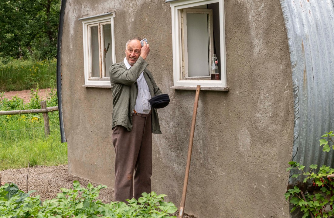 Mann steht vor einer Nissenhütte und wischt sich den Schweiß von der Stirn.