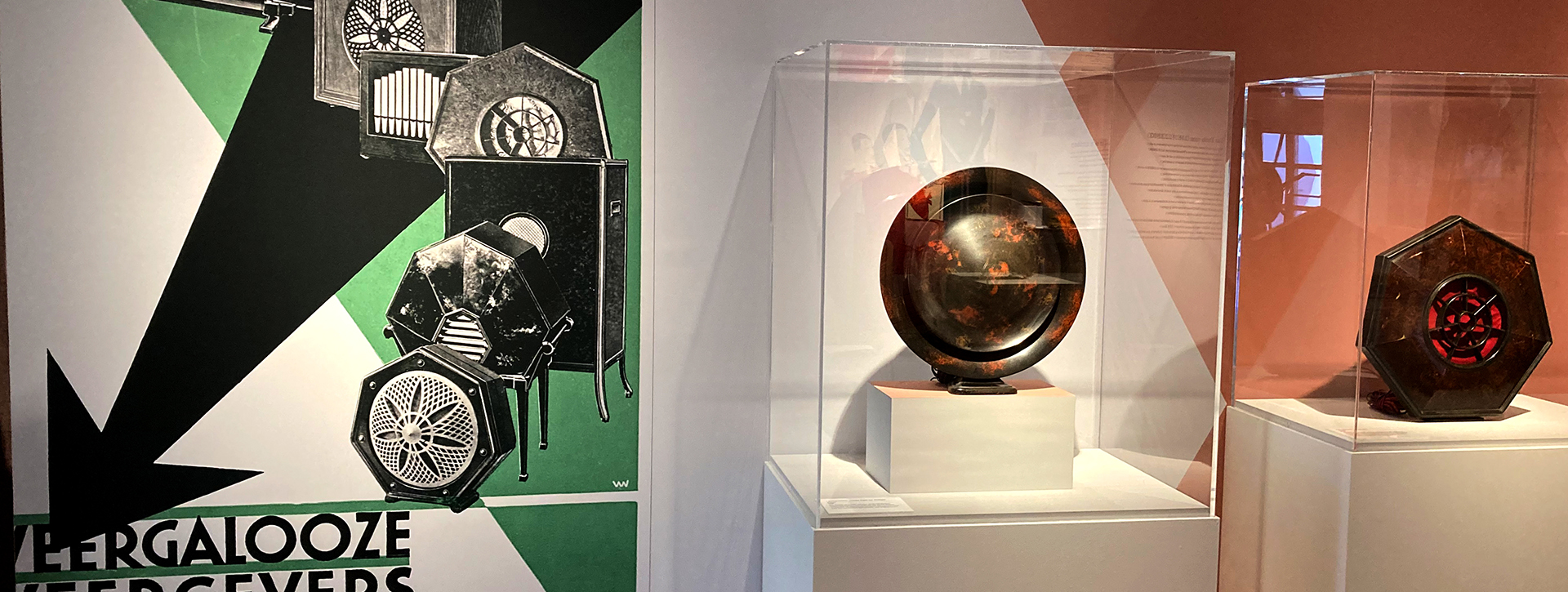 Blick in die Ausstellung mit altem Werbeplakat zu Lautsprechern, daneben in einer Vitrine dieselben Lautsprecher als Objekt aus Bakelit