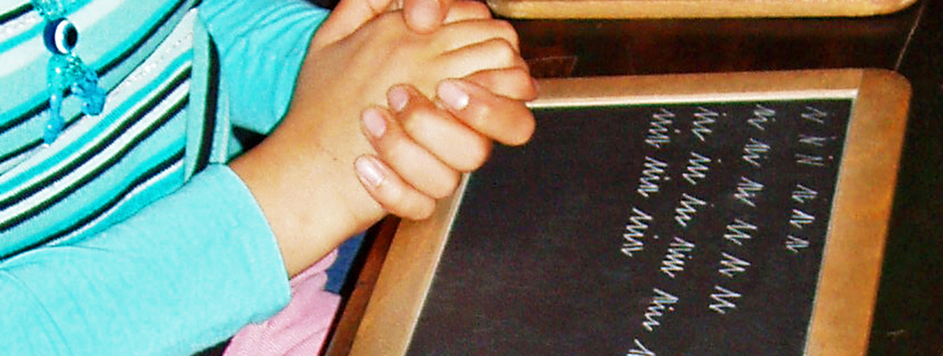 Gefalltete Kinderhand vor einer Schiefertafel