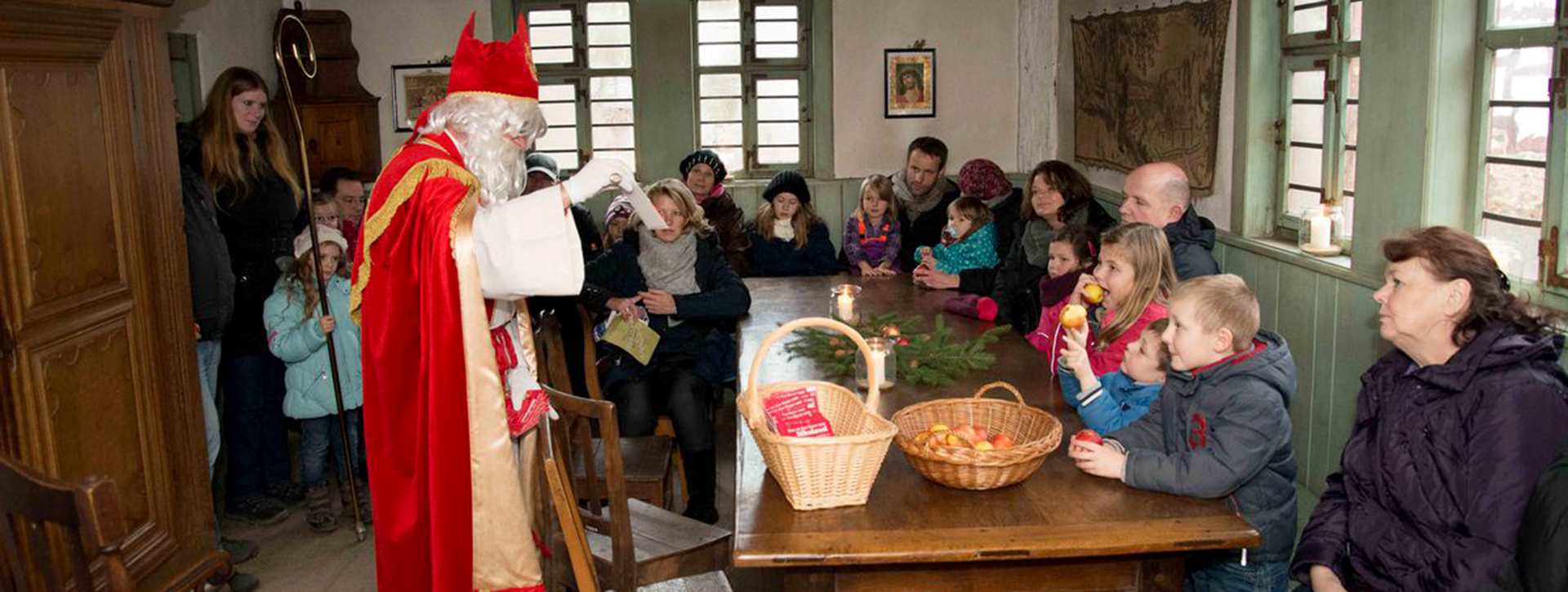 Nikolaus im roten Mantel spricht mit Kindern, die an einem Tisch sitzen