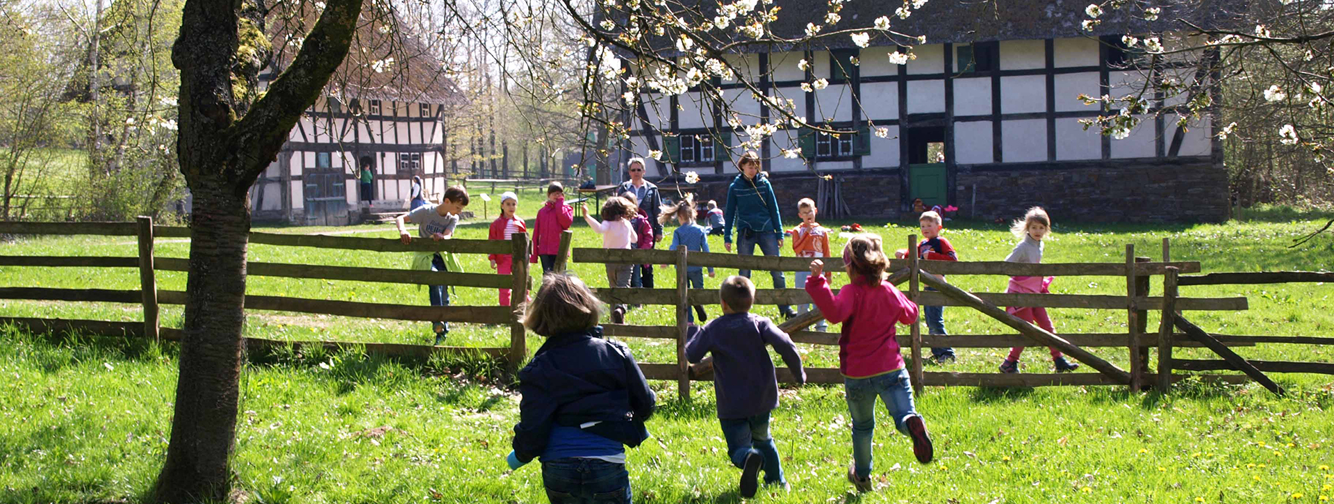 Children run across a meadow towards half-timbered houses