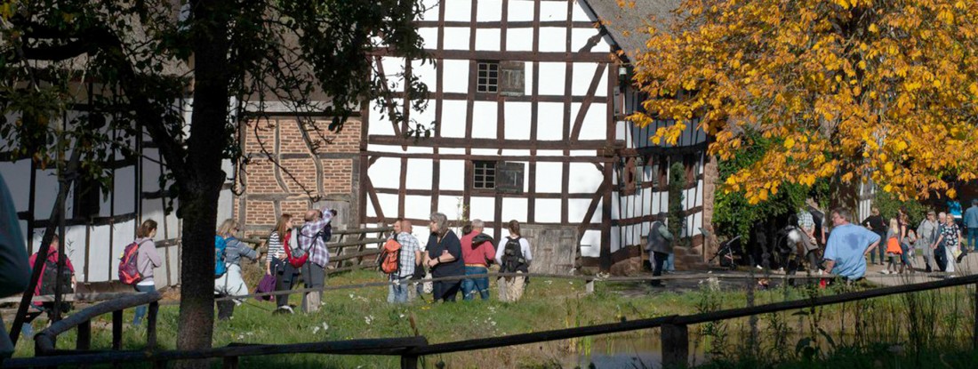 Weg mit Menschen, daneben Fachwerkhäuser und Bäume mit roten Blättern