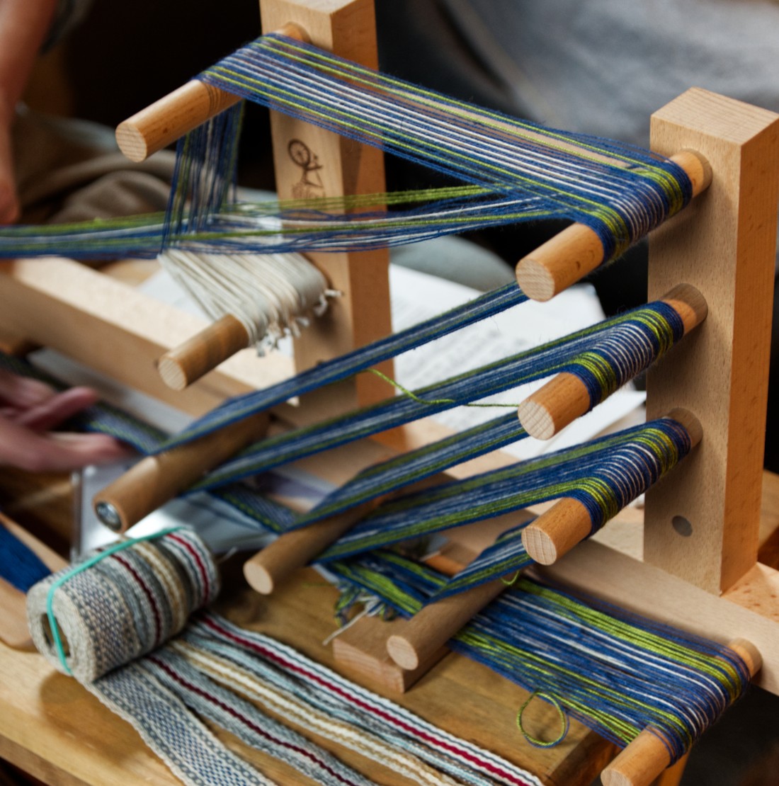 A man loads hay onto a cart pulled by a goat. A woman leads the goat