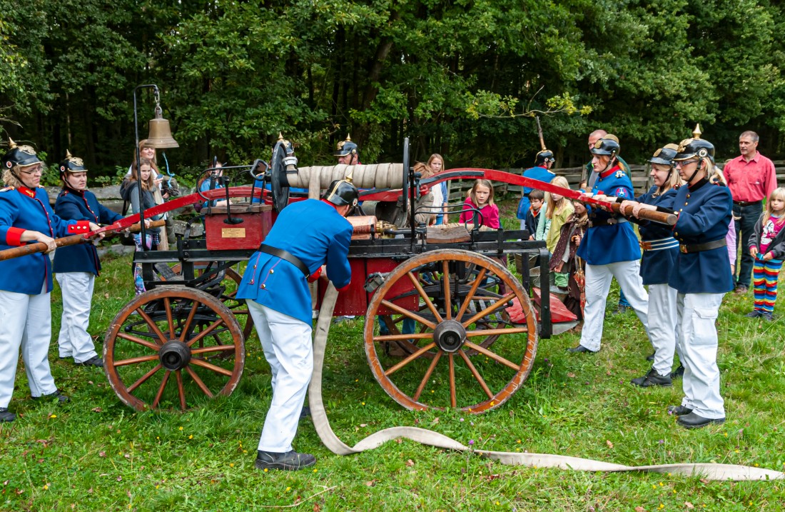 Historisch gekleidete Männer mit einem hölzernen Feuerwehrwagen