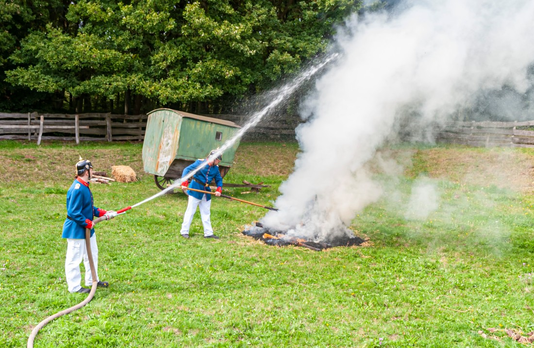 Historically dressed men extinguish a fire with a hose