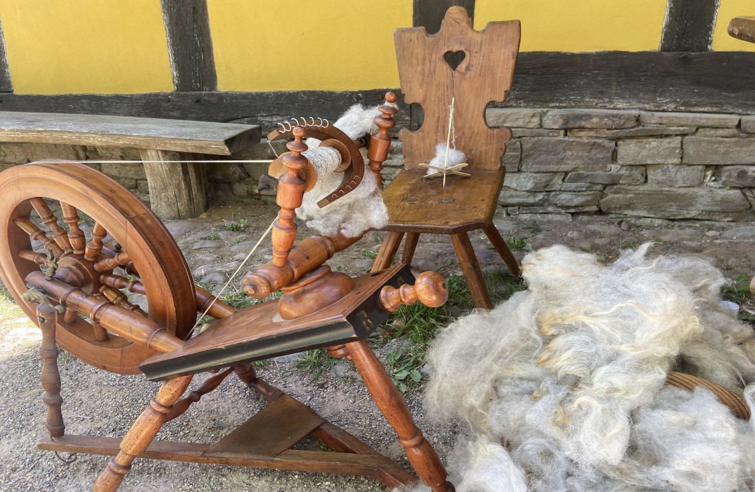A spinning wheel stands in front of a half-timbered building. Behind it a chair with a hand spindle.