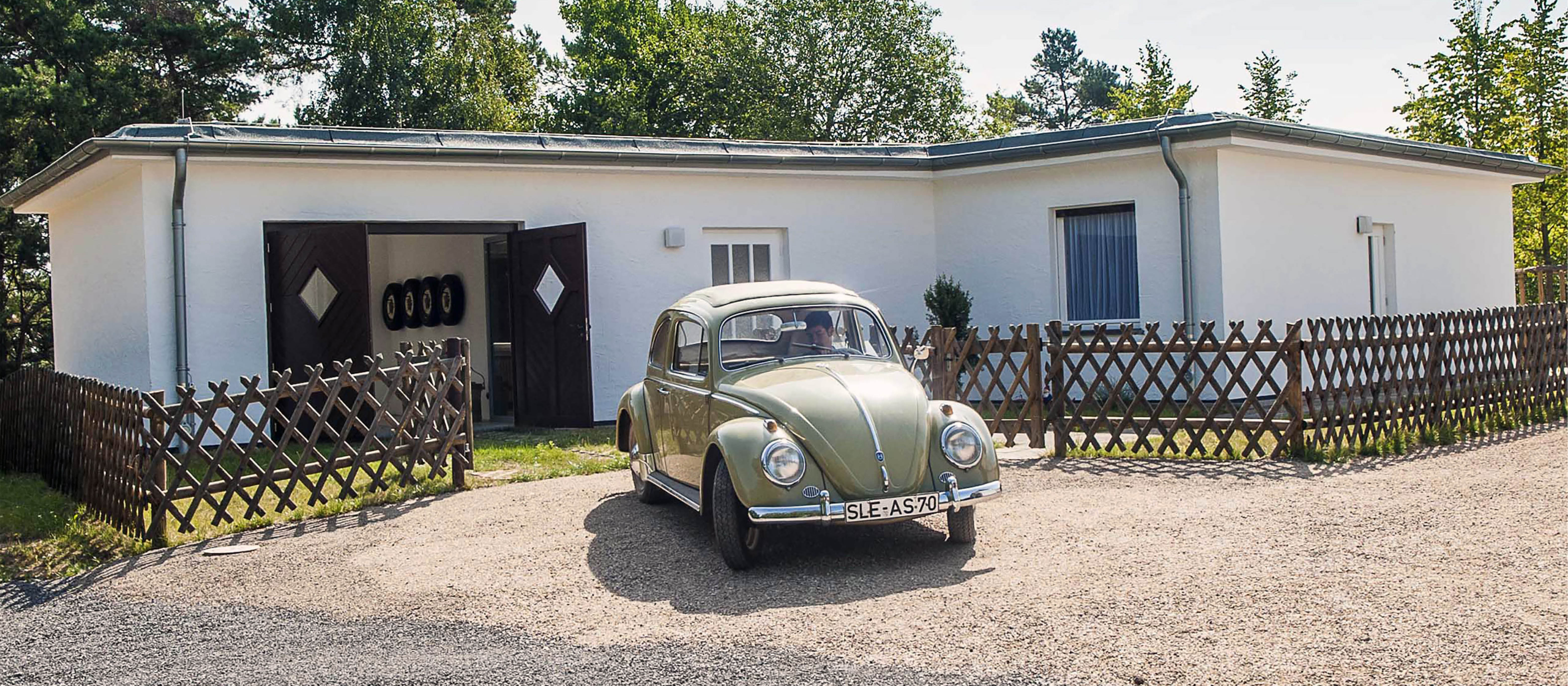 Alter VW-Käfer vor einem weißen Bungalow