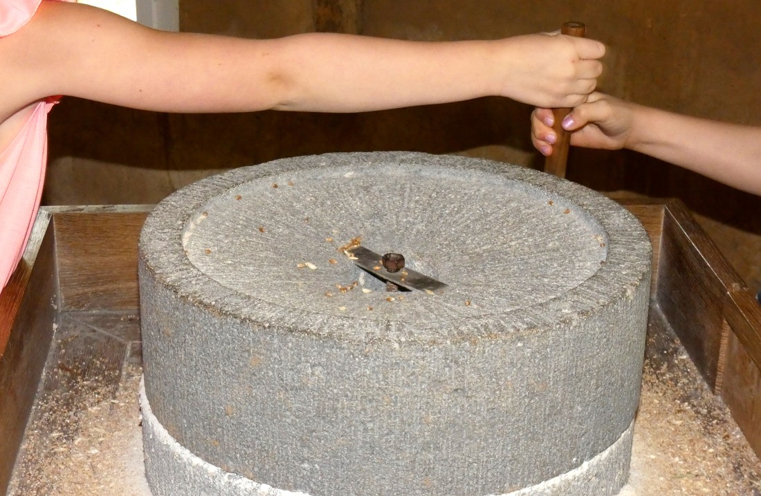 Ein Mahlstein wird von Kinderhänden gedreht