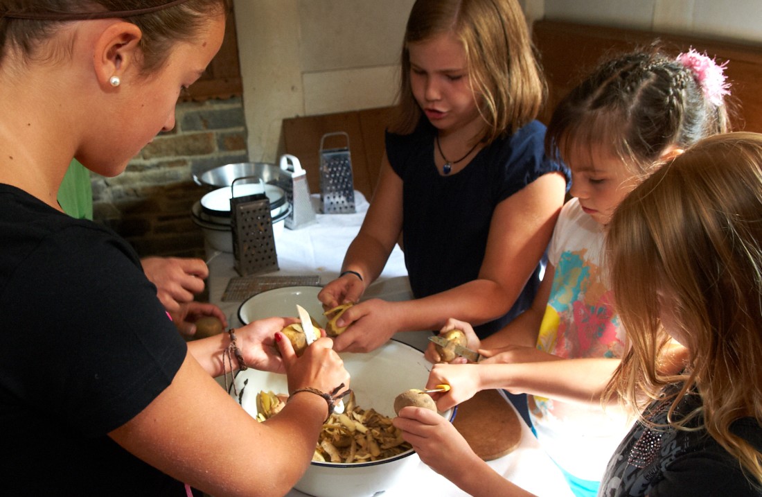 Kinder stehen um einen Tisch und schälen Kartoffeln
