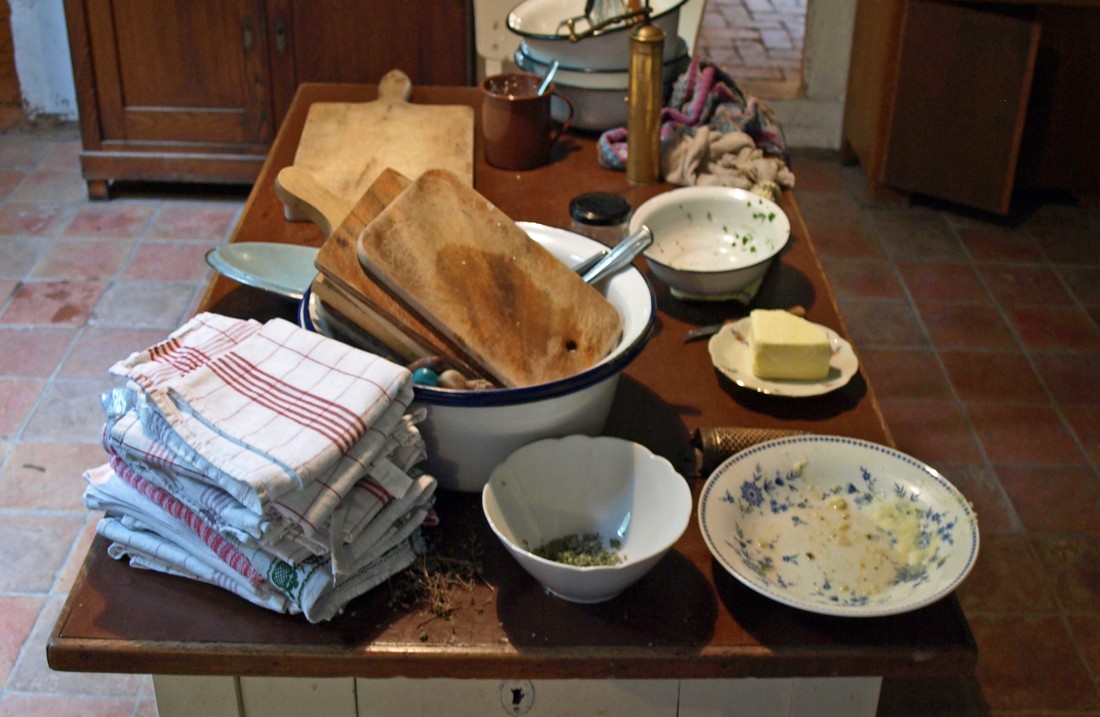 Tisch mit Küchentüchern, Schüsseln, Schnedebrttern, Butter und anderen Kochutensilien
