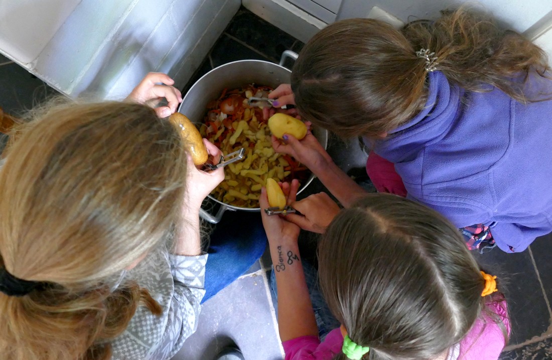 Children bend over a saucepan and peel potatoes