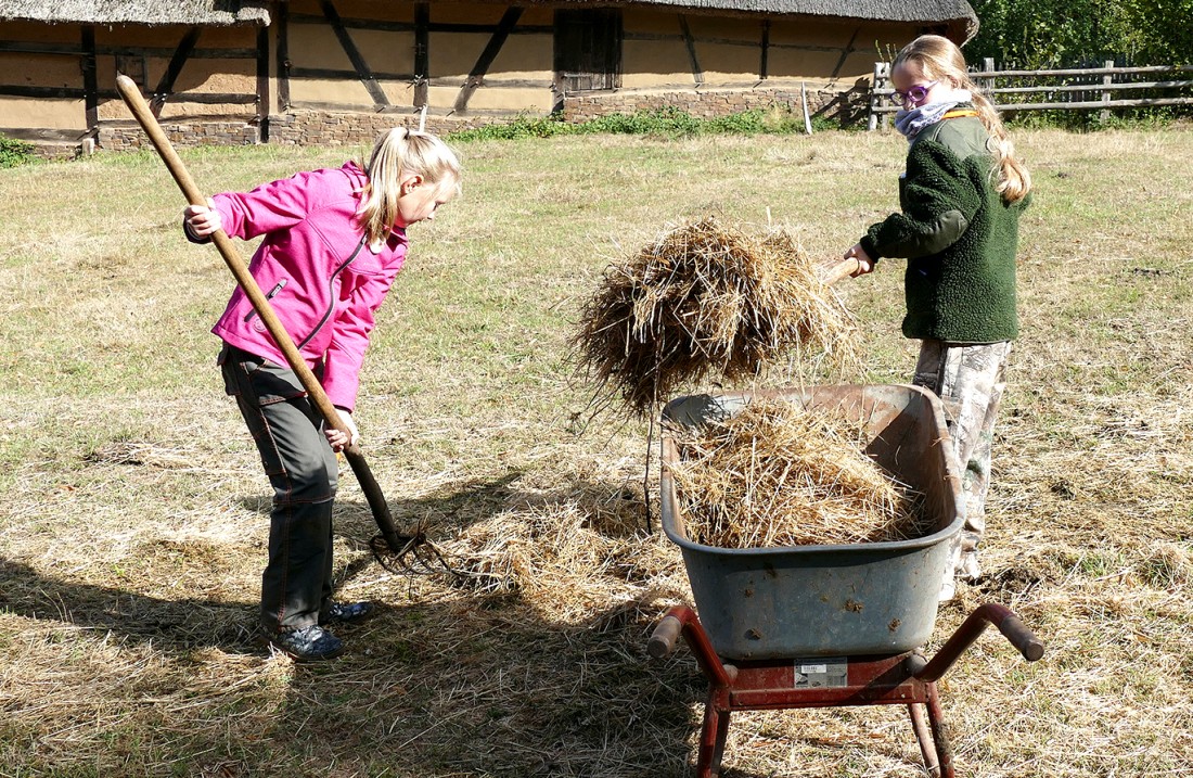 Two girls lift hay into a wheelbarrow