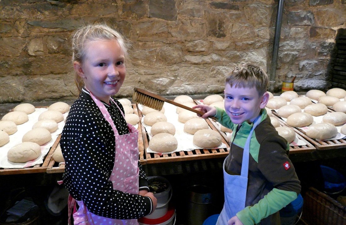 A girl and a boy stand in front of pallets with un -chopped rolls and look into the camera